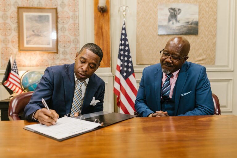One man signing a piece of paper while another man looks on.