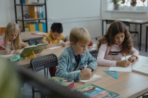 three children sitting in a classroom working on a school assignment.