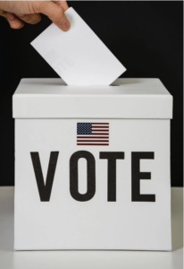 A white box with an American flag above the words VOTE and a ballot being placed in the box