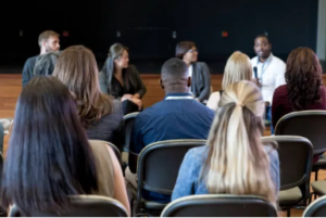 back view of audience listening to 3 people, with one holding a microphone