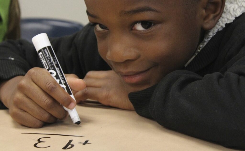 Black boy grinning at camera as he holds a magic marker in his hand drawing numbers