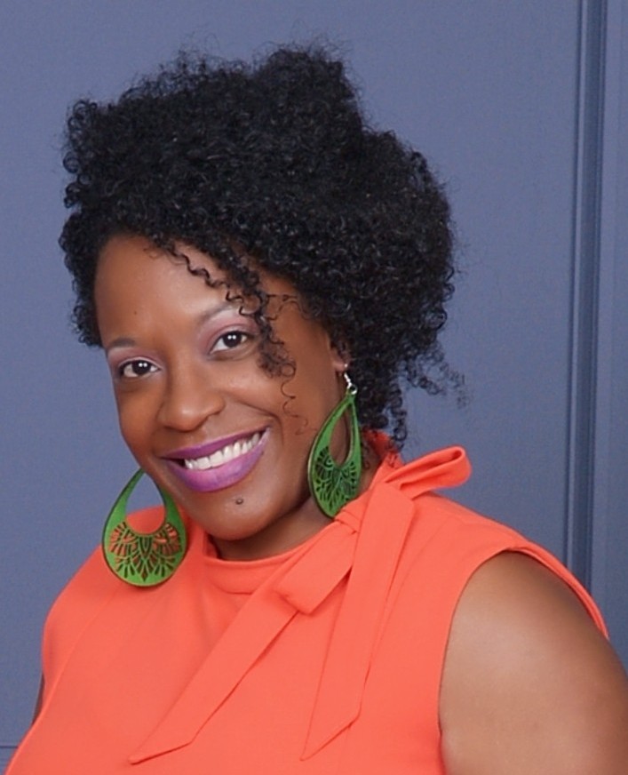 Black woman with hair in updo and large green earrings smiling at camera