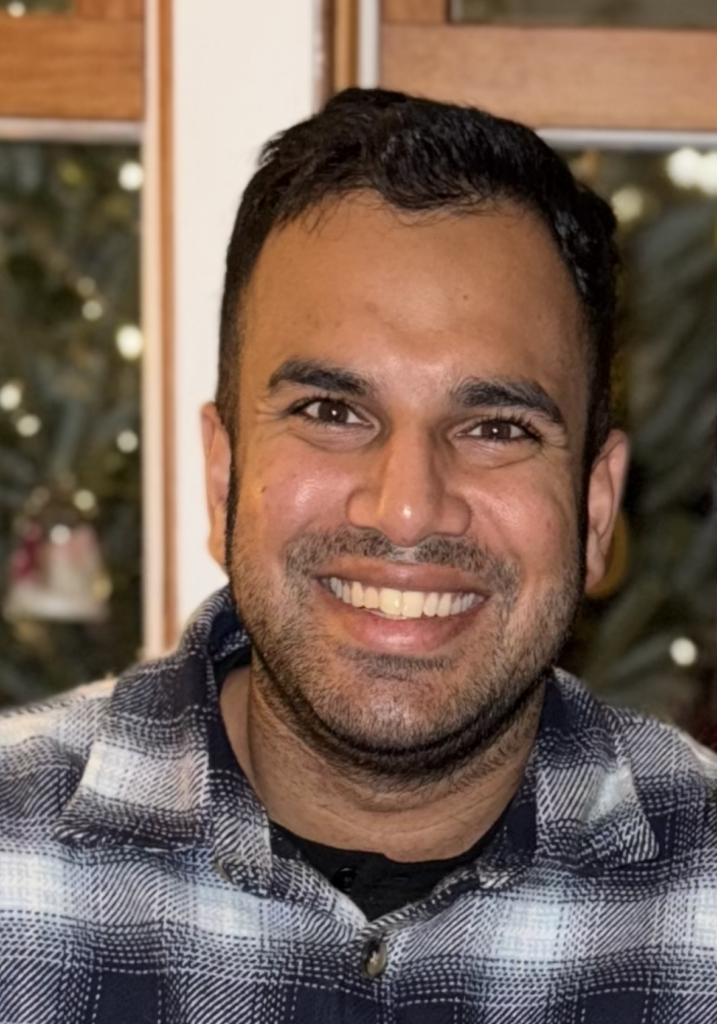 Dark-skinned young man with stubble beard smiles at the camera