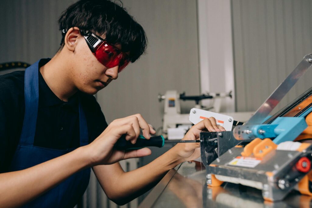 Young man wearing safety glasses using a screwdriver to fix a machine.